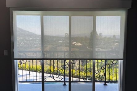 Patio doors in a San Jose home dressed with custom sheer roller shades, showcasing a scenic outdoor view and decorative railing.